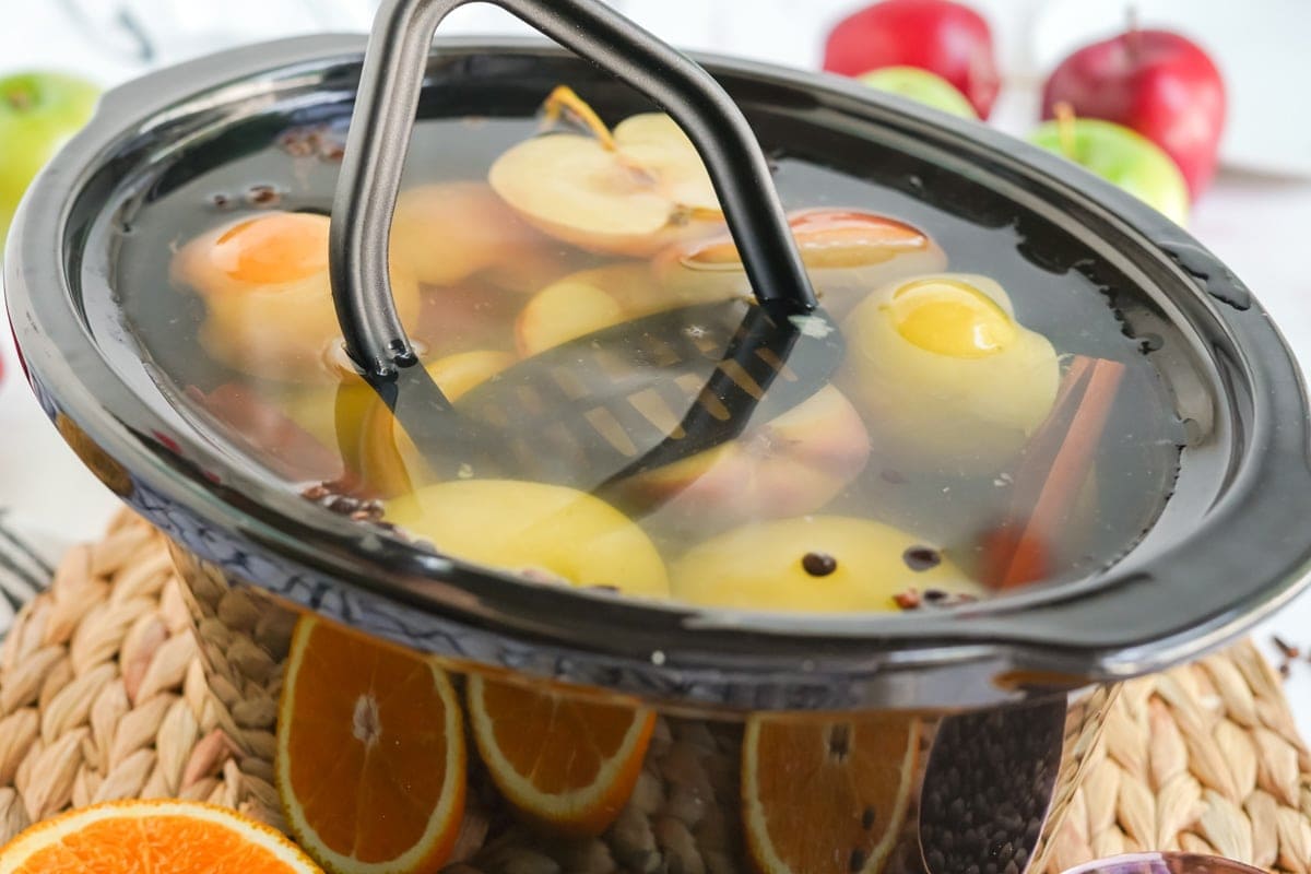 potato masher in a crock pot of apples and water