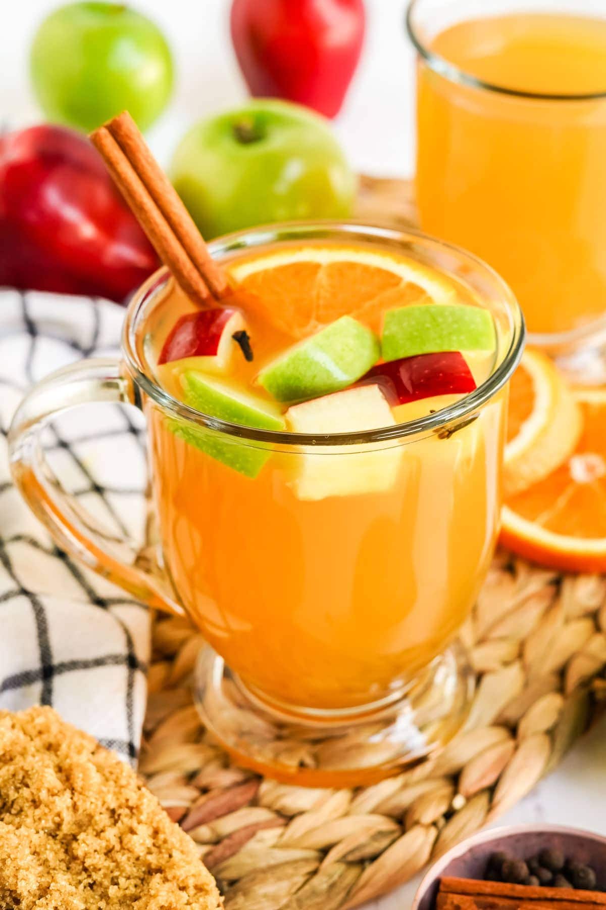 apple cider in a clear glass mug with apple chunks and a cinnamon stick