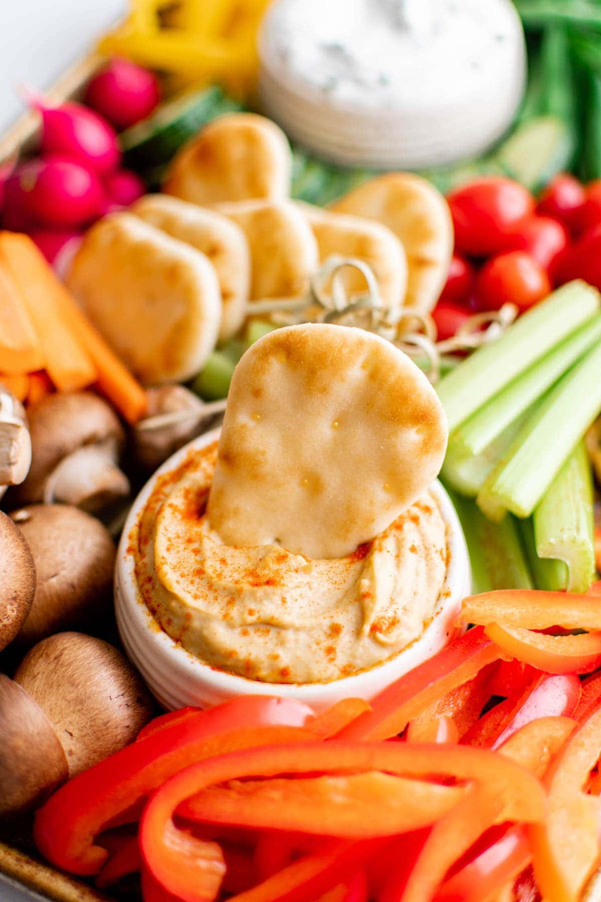 pita bread dipped in hummus surrounded by vegetables on a trray