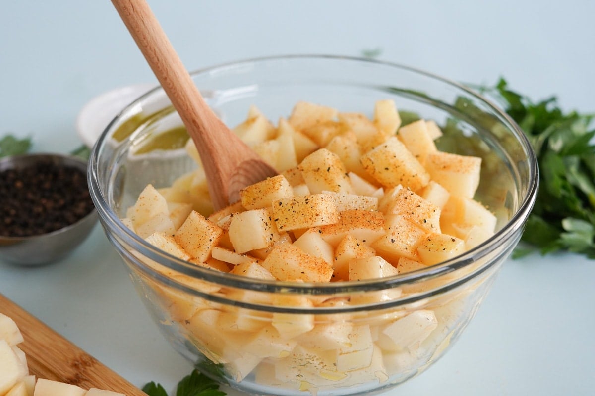 cut up potatoes in a bowl with a wood spoon and seasoning