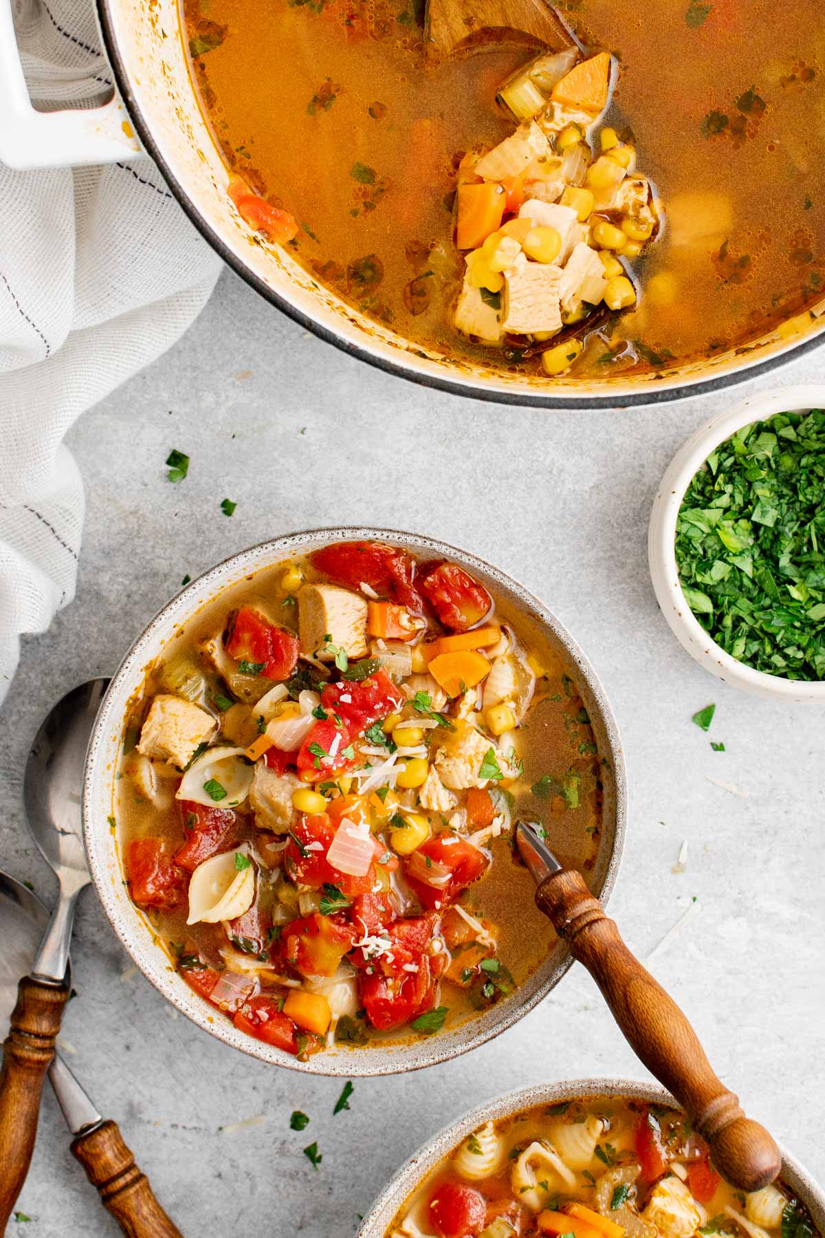 chicken vegetable soup in a hwite bowl, spoon, white pot