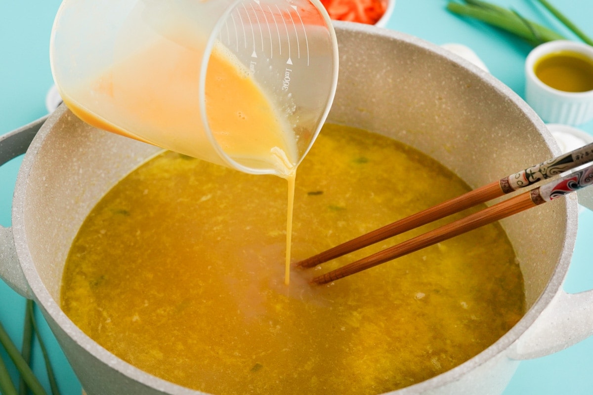 beaten eggs pouring into pot of soup