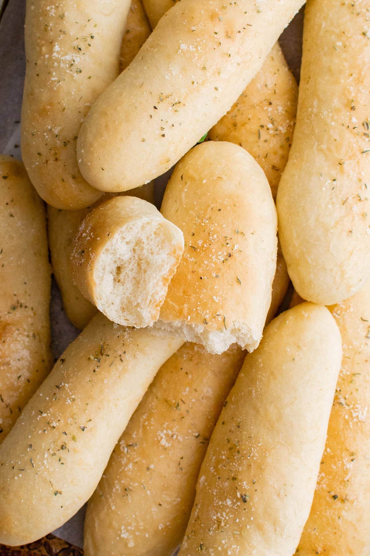 pile of garlic breadsticks, one broken in half to reveal the fluffy interior