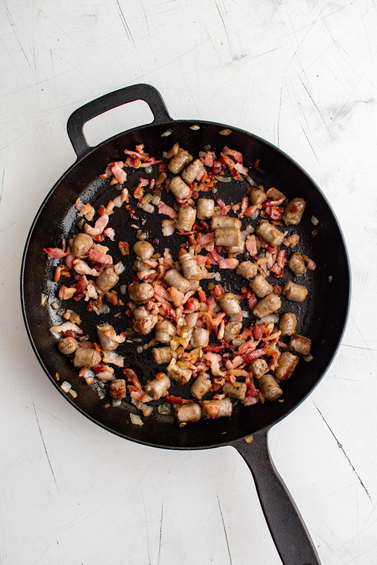 sausage, bacon and onions in a cast iron skillet