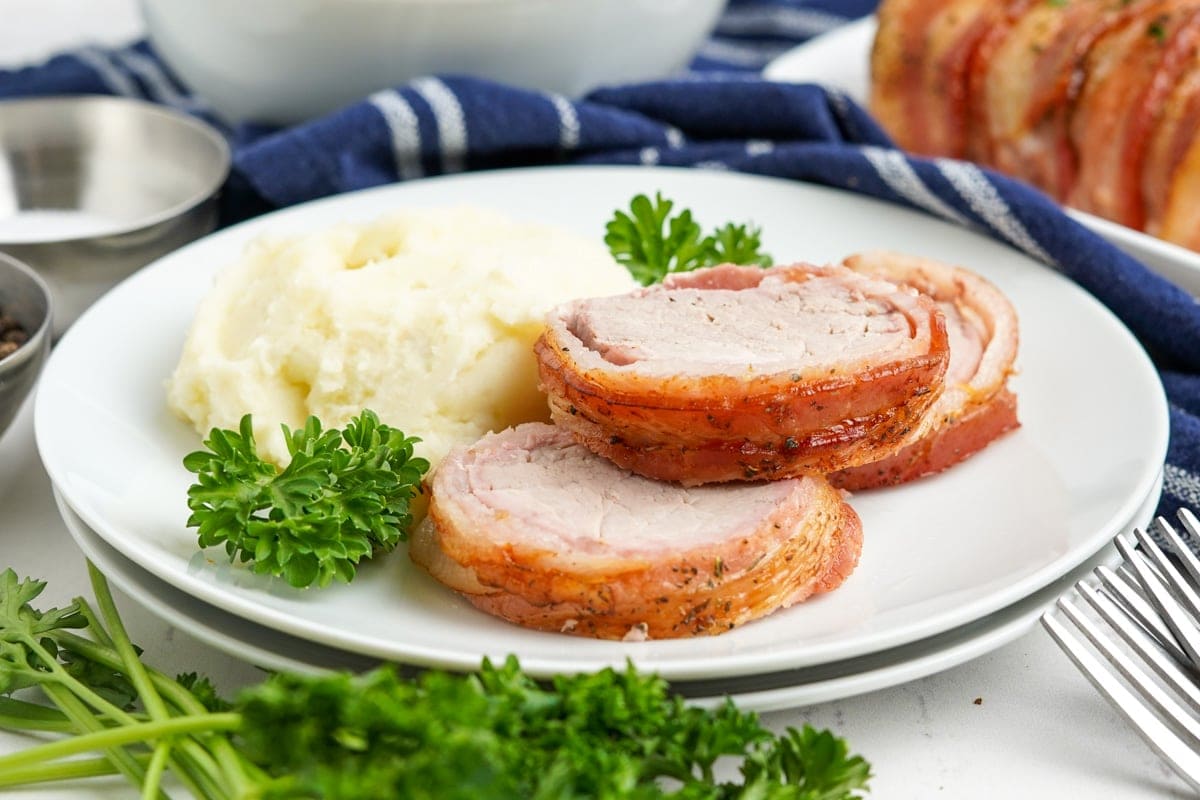 slices of pork wrapped in bacon on a plate with mashed potatoes