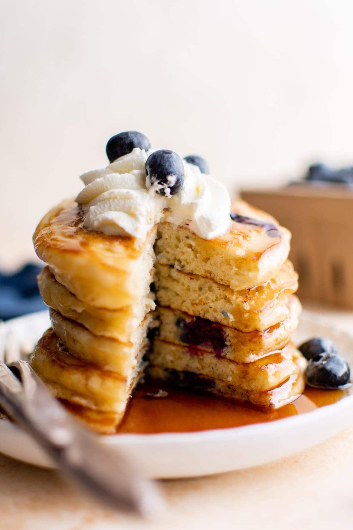stack of blueberry pancakes cut open, topped with whipped cream