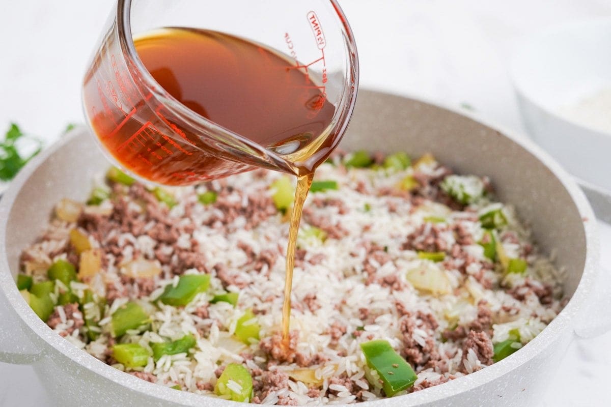 beef broth poured in a pot of rice and ground beef