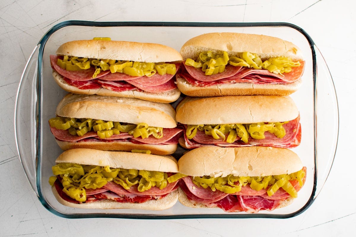 hoagie rolls in a baking dish with salami, ham, and banana peppers