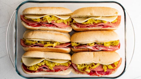 sub sandwiches with italian meat, banana peppers and sliced cheese in a baking dish