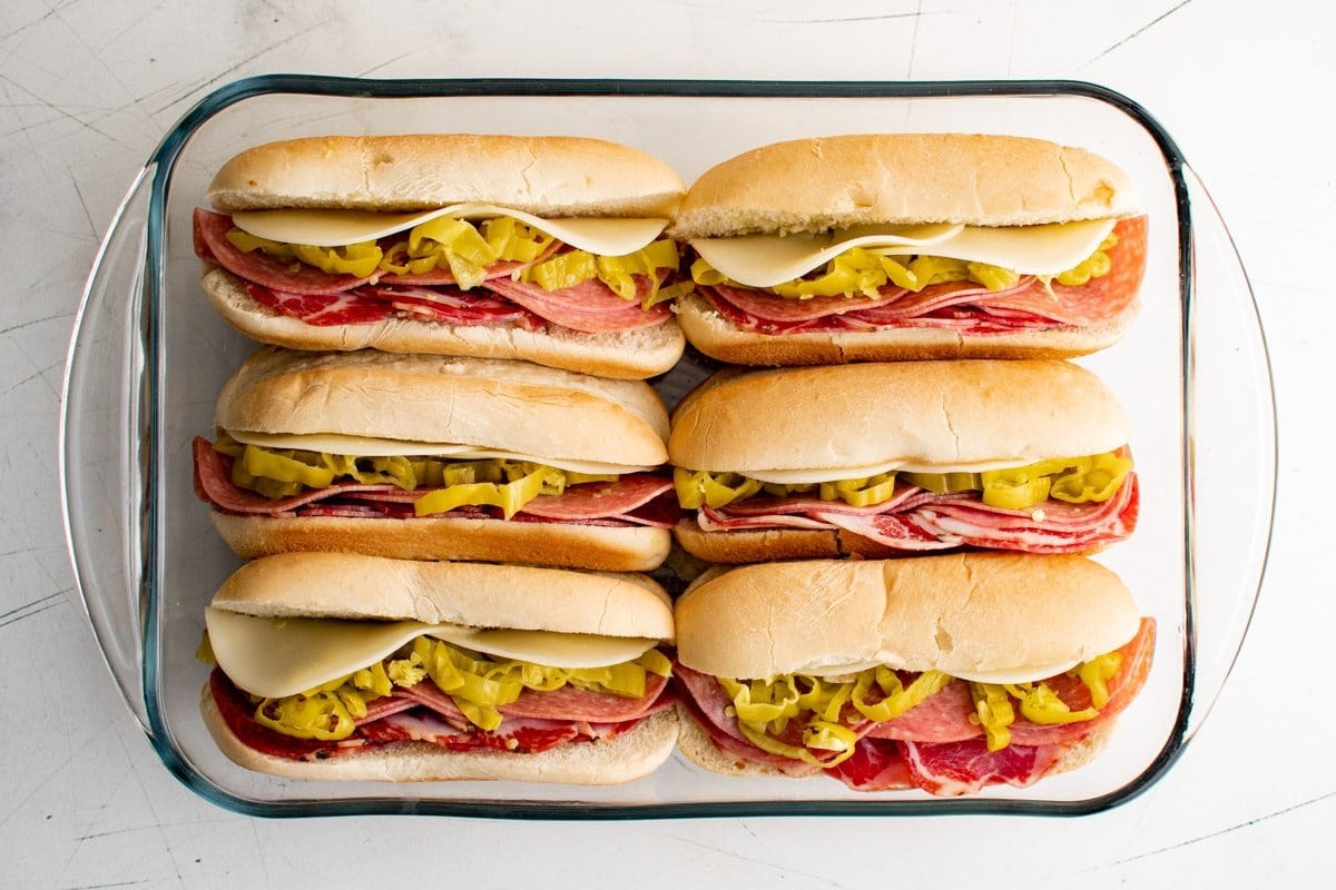 sub sandwiches with italian meat, banana peppers and sliced cheese in a baking dish