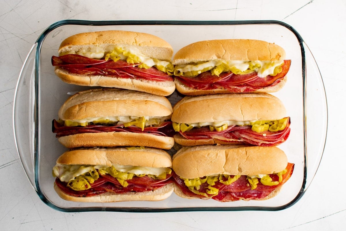 baked sub sandwiches with italian meat, banana peppers and melted cheese in a baking dish