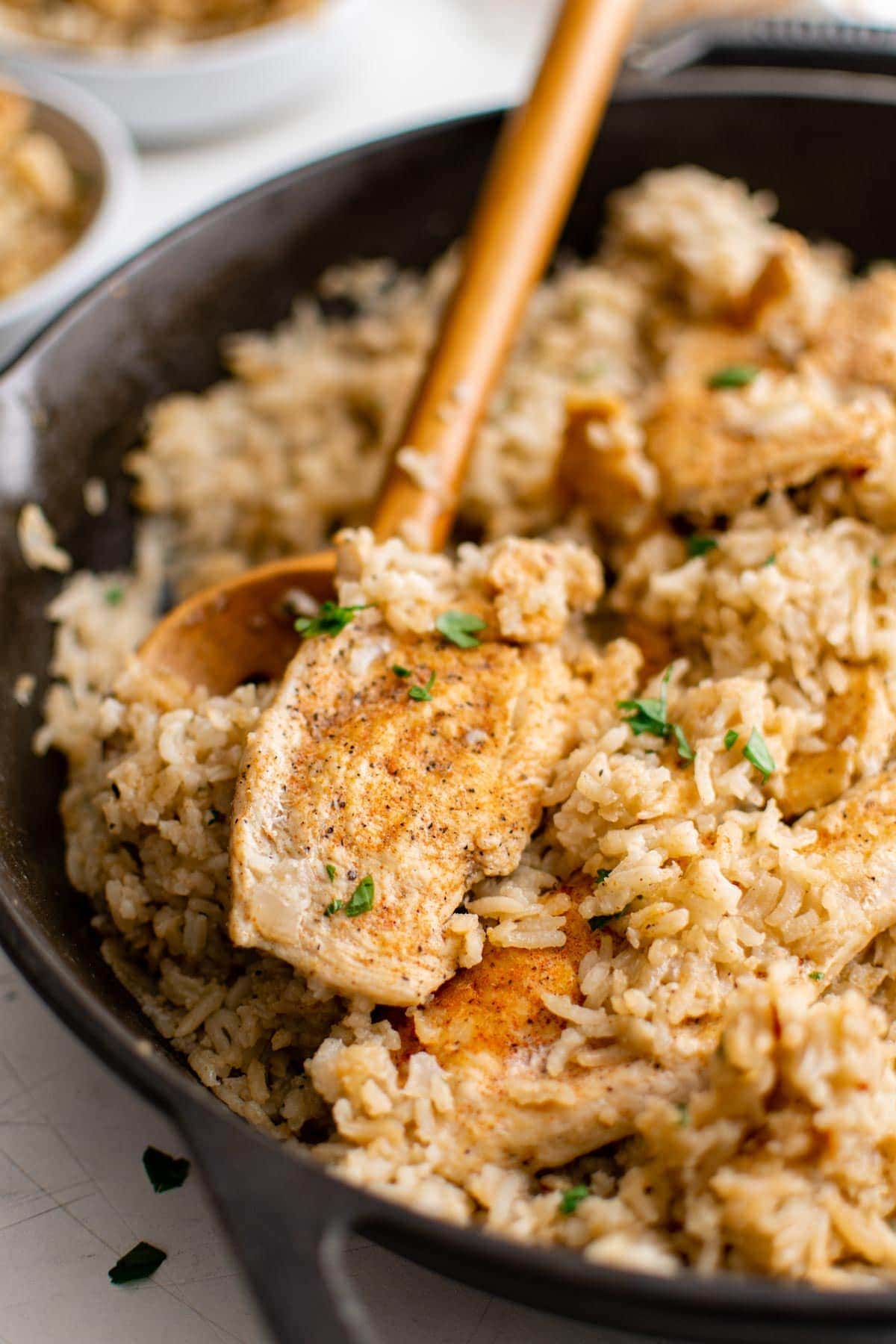 wooden spoon, chicken breast, rice in a skillet