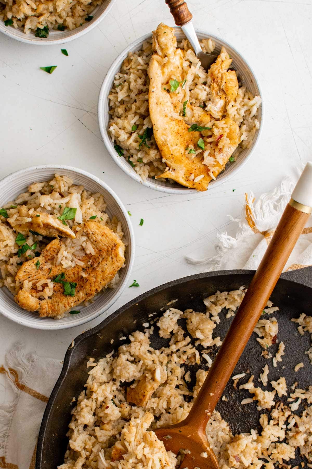 chicken and rice casserole in white bowls, skillet with rice and a wooden spoon