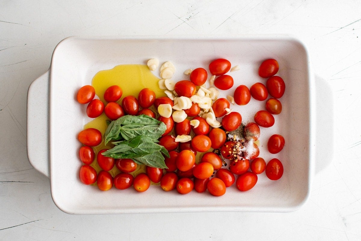 cherry tomatoes, basil, garlic and olive oil in a white baking dish