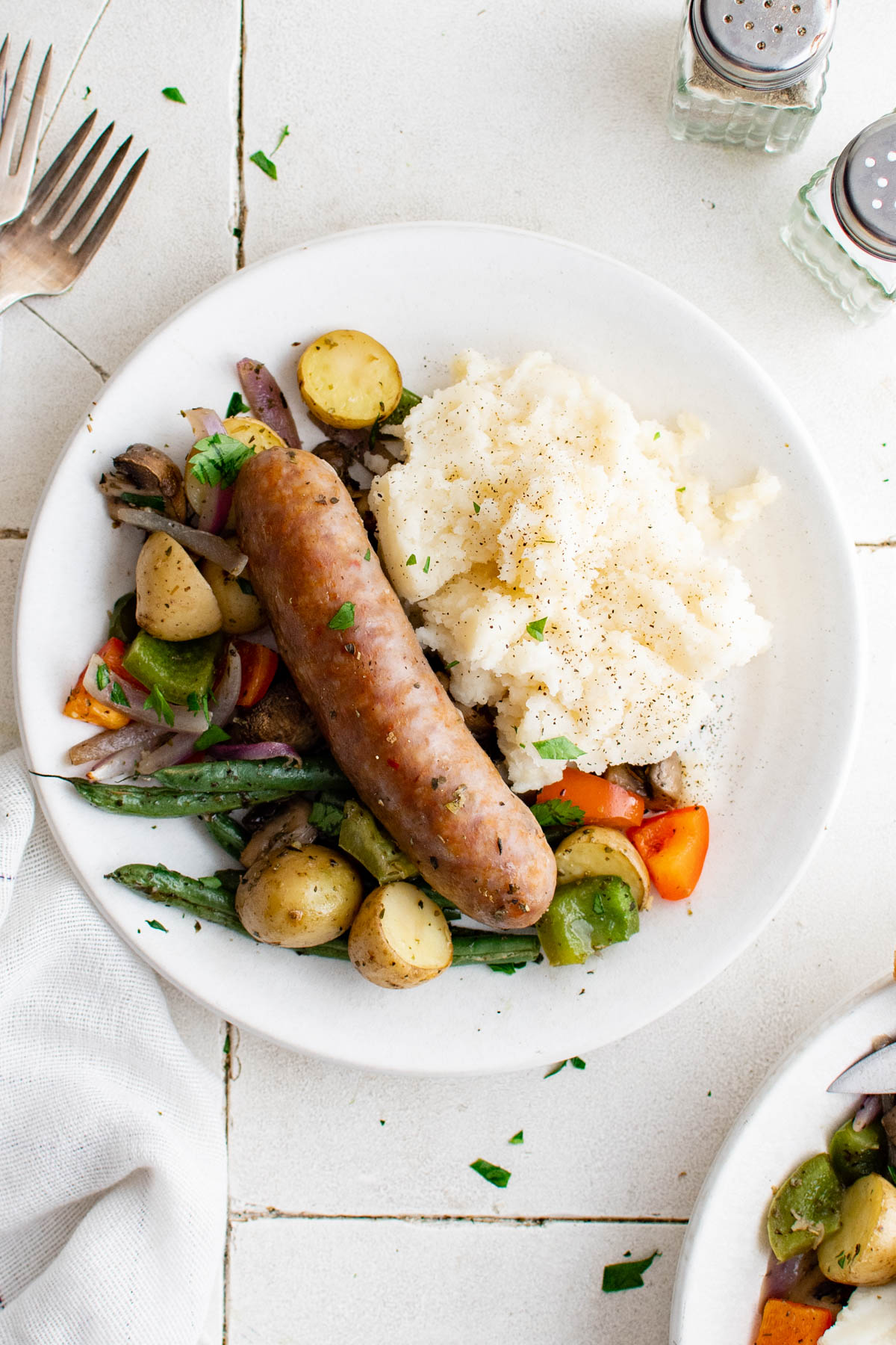 white plate with one sausage, veggies and mashed potatoes