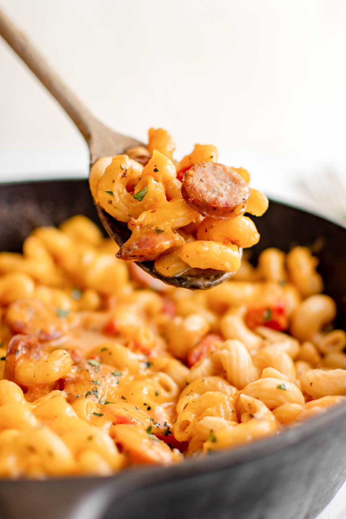 sausage mac and cheese in a skillet with a wooden spoon