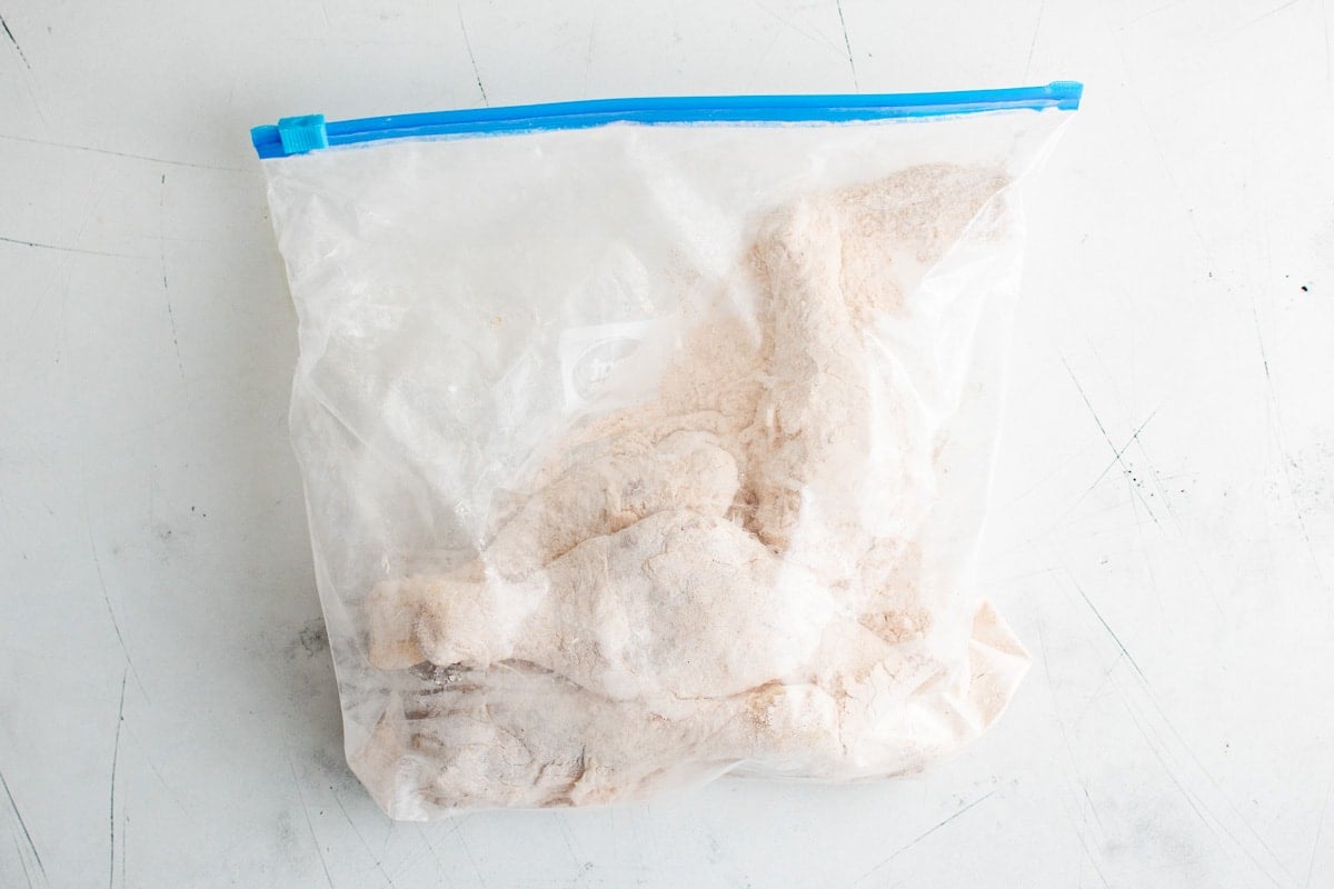 Chicken legs in a plastic bag, coated in flour and seasonings.