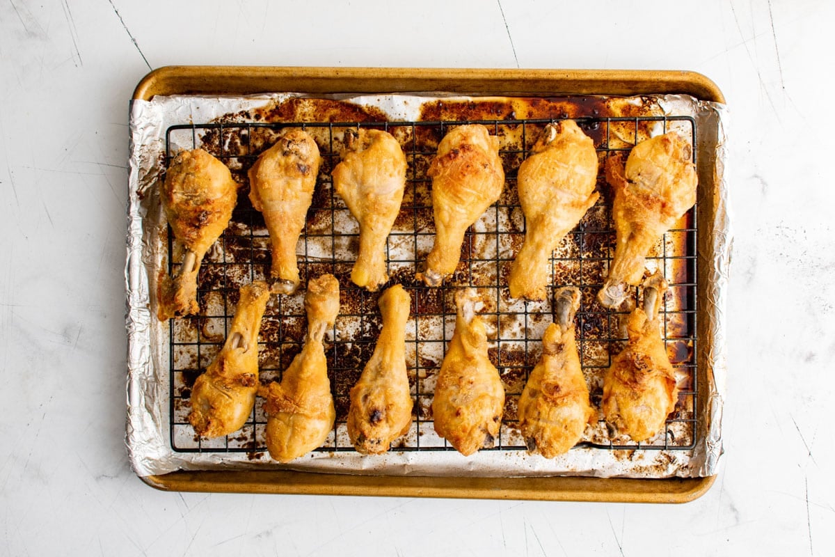 Baked and browned chicken drumsticks on a baking sheet.