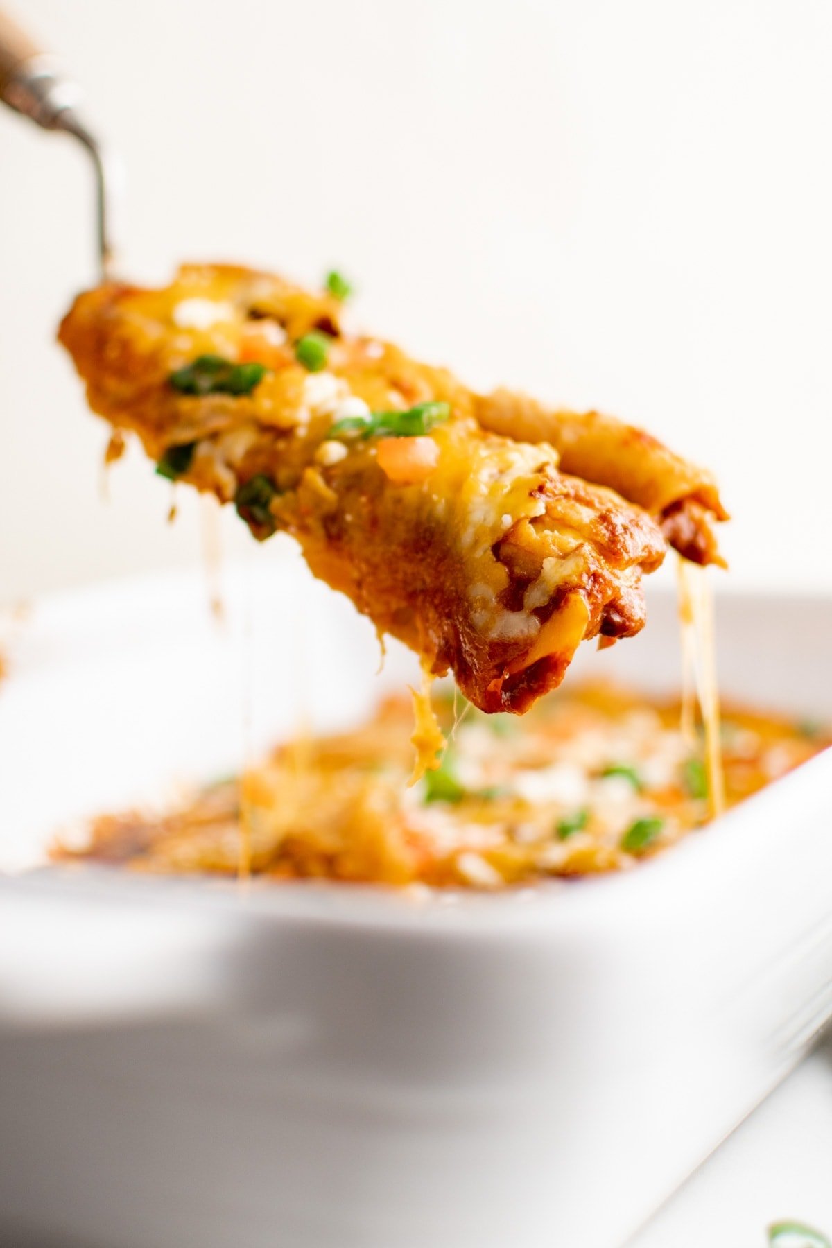 enchiladas being lifted out of a baking pan