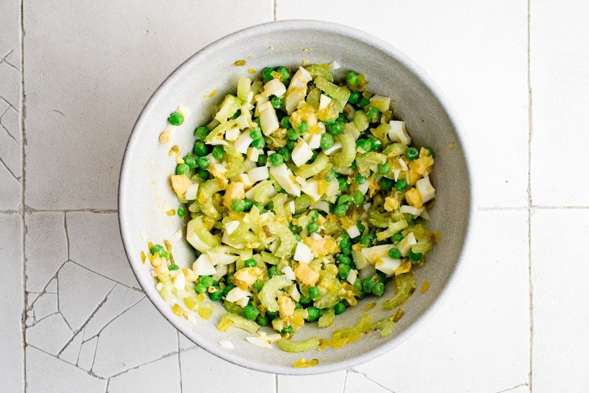 Peas, hard boiled eggs, celery, and onions combined in a bowl.