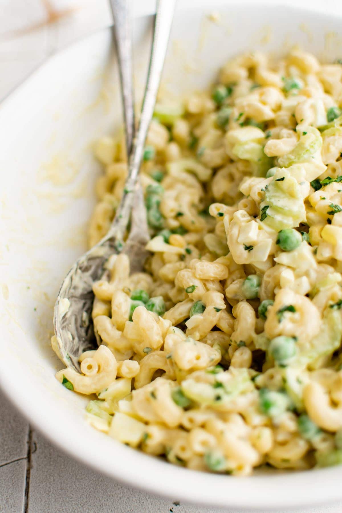 macaroni salad in a white bowl with metal spoons