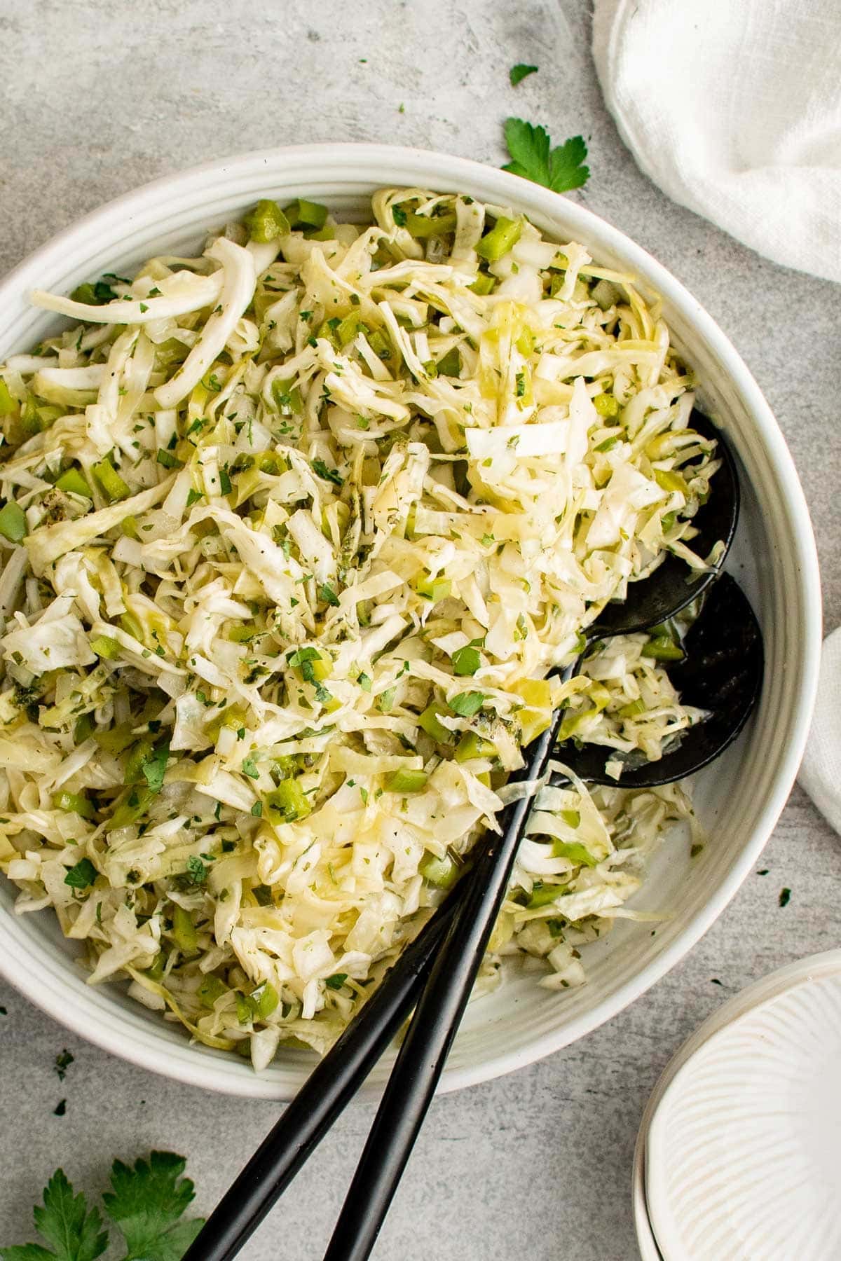 large white bowl with green cabbage salad and black spoons