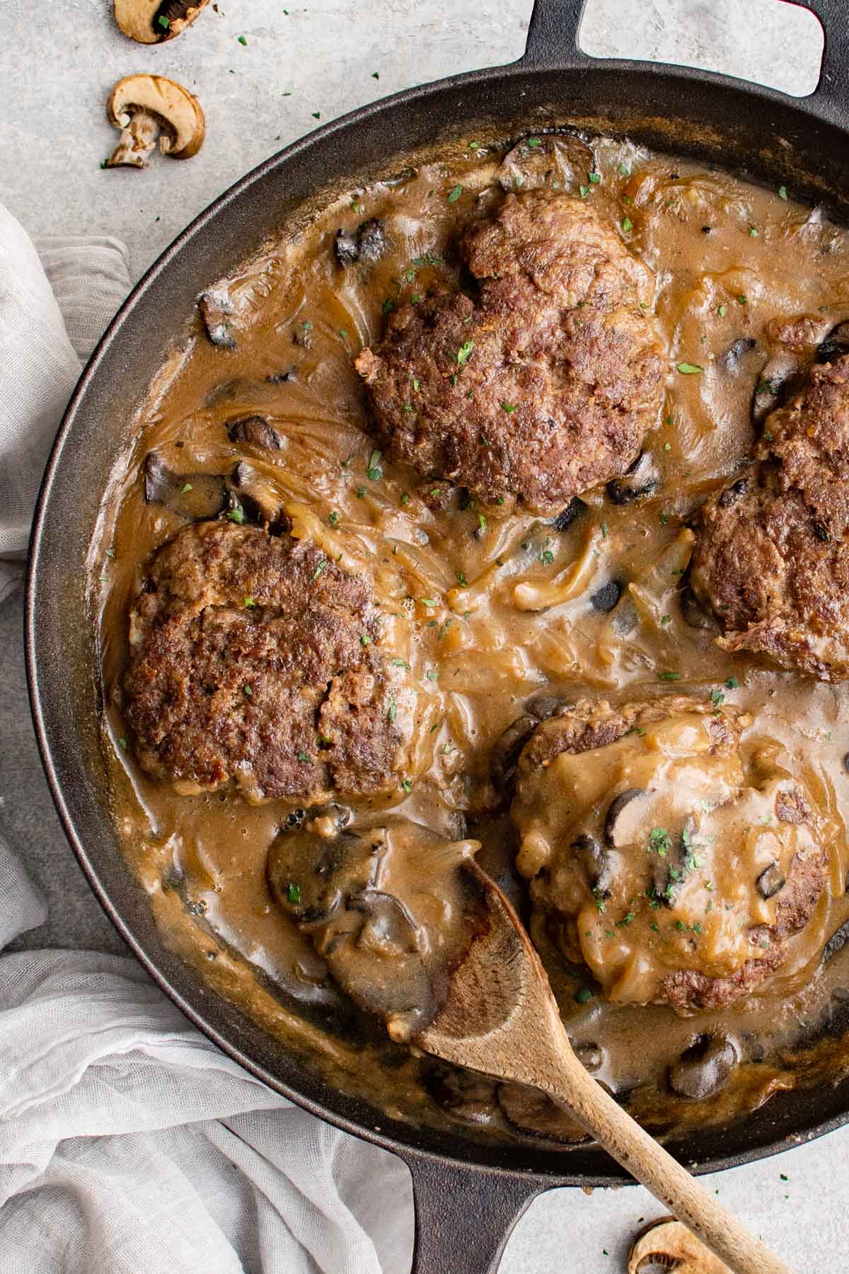 chopped steaks in a skillet with gracy, onions and mushrooms, a wooden spoon