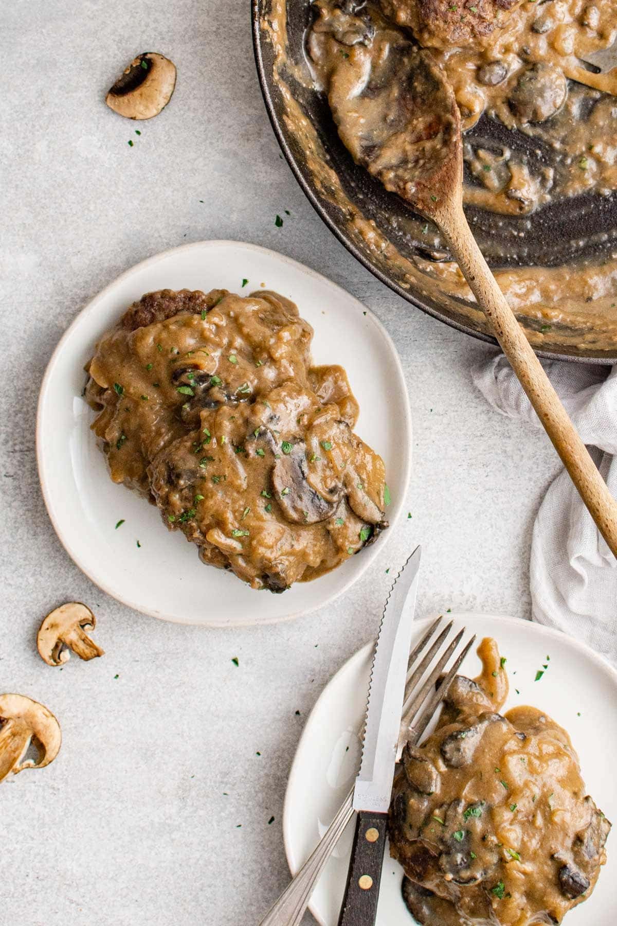 chopped beef steaks on white plates and with gravy, fork and steak knives