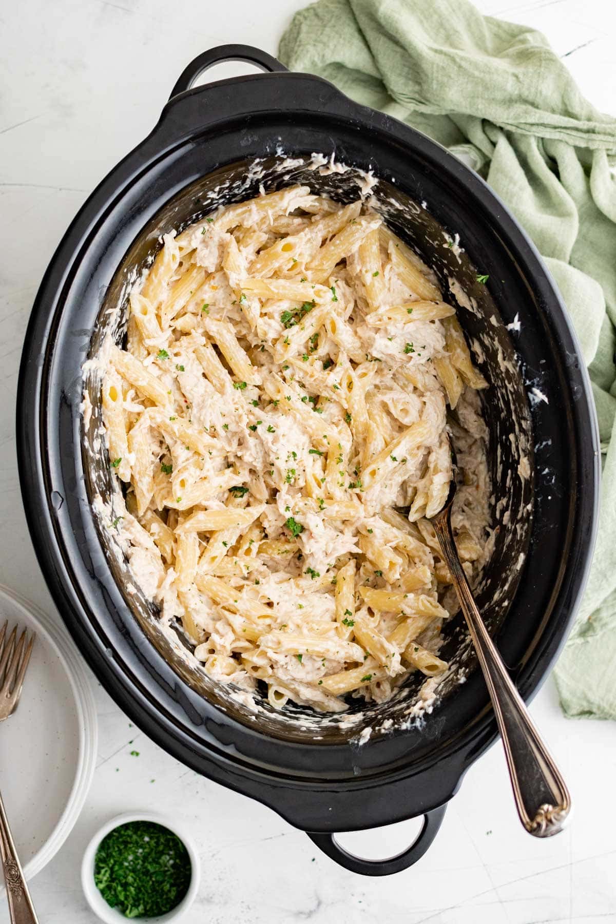 Penne pasta with cheese and a creamy sauce in a slow cooker with a spoon.