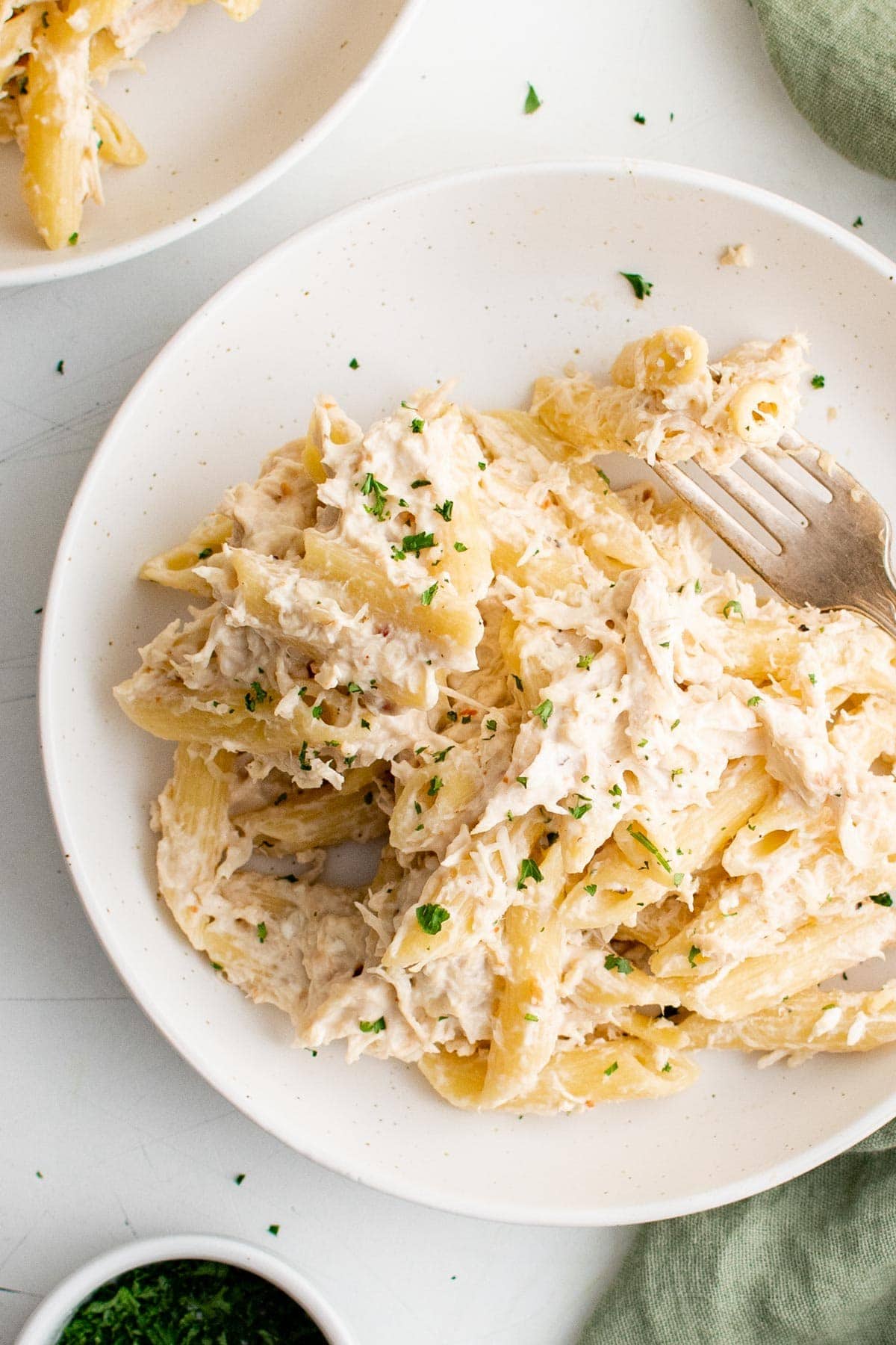 penne pasta and cheese and a cream sauce with parsley on a white plate.