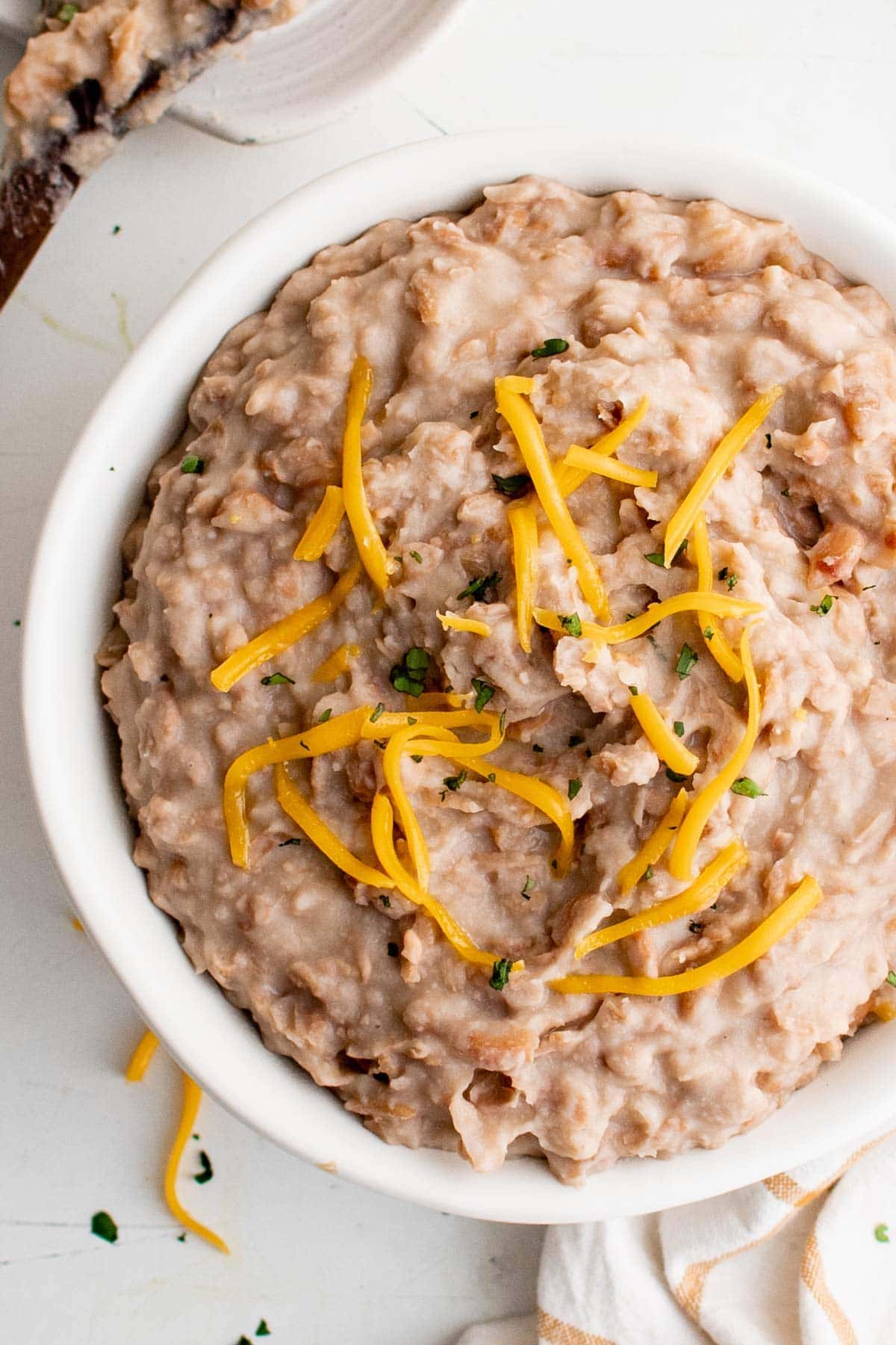 a large white bowl filled with refried beans topped with shredded cheese
