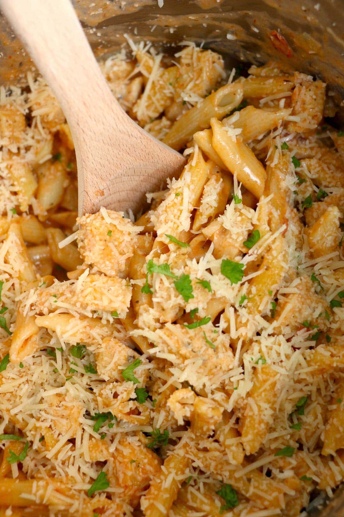 Cream tomato sauce with pasta and chicken and a wooden spoon in an instant pot. 