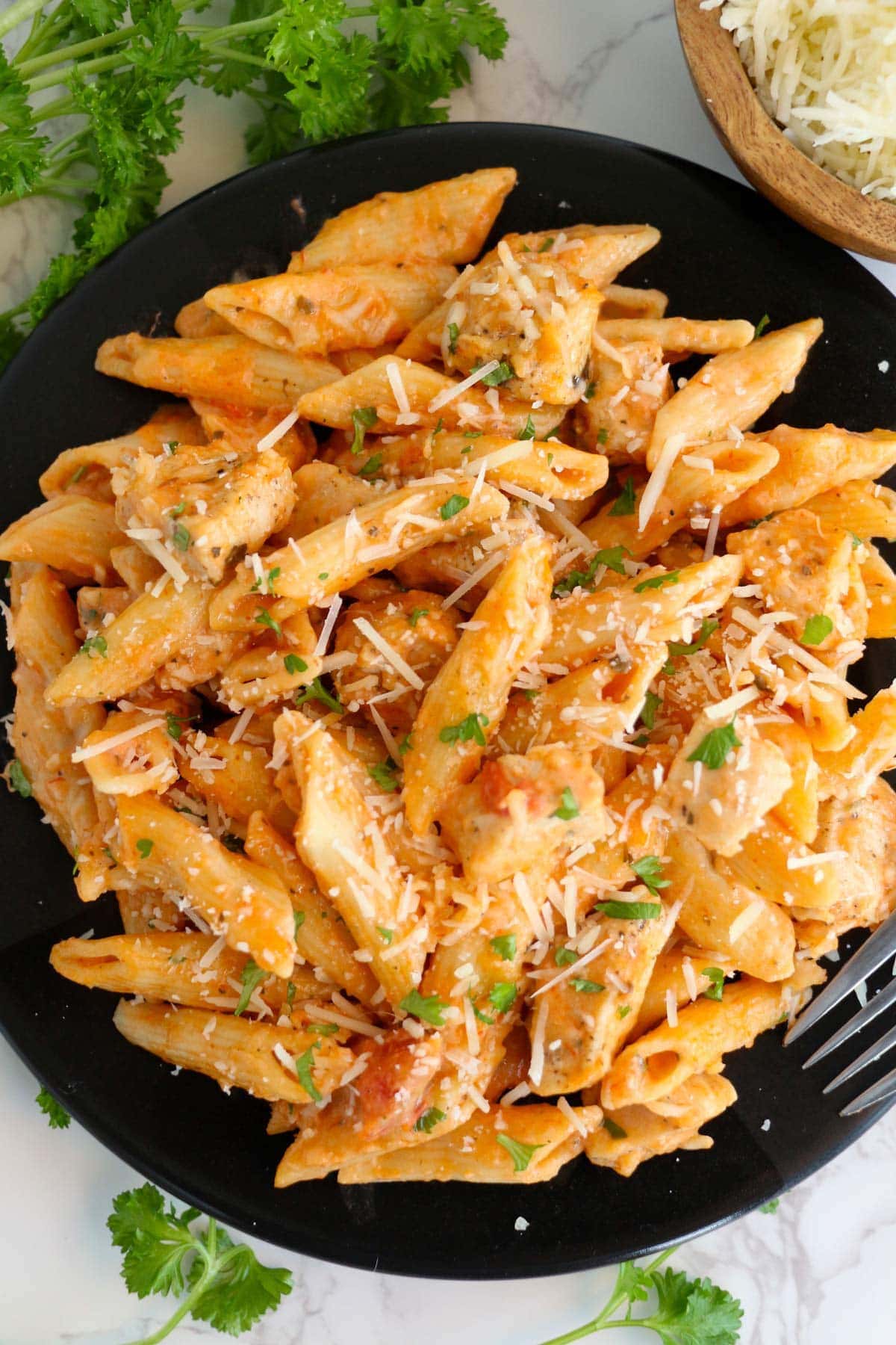 a black plate surrounded by parsley, with penne pasta dn chicken in a creamy tomato sauce