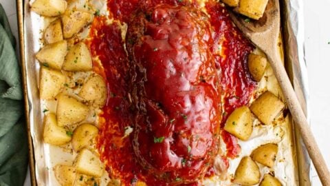 meatloaf with sauce, surrounded by potatoes on a sheet pan