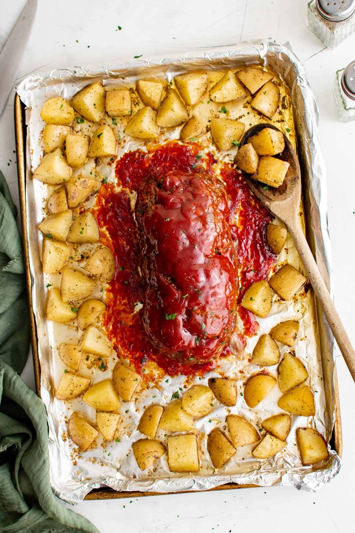 meatloaf with sauce, surrounded by potatoes on a sheet pan