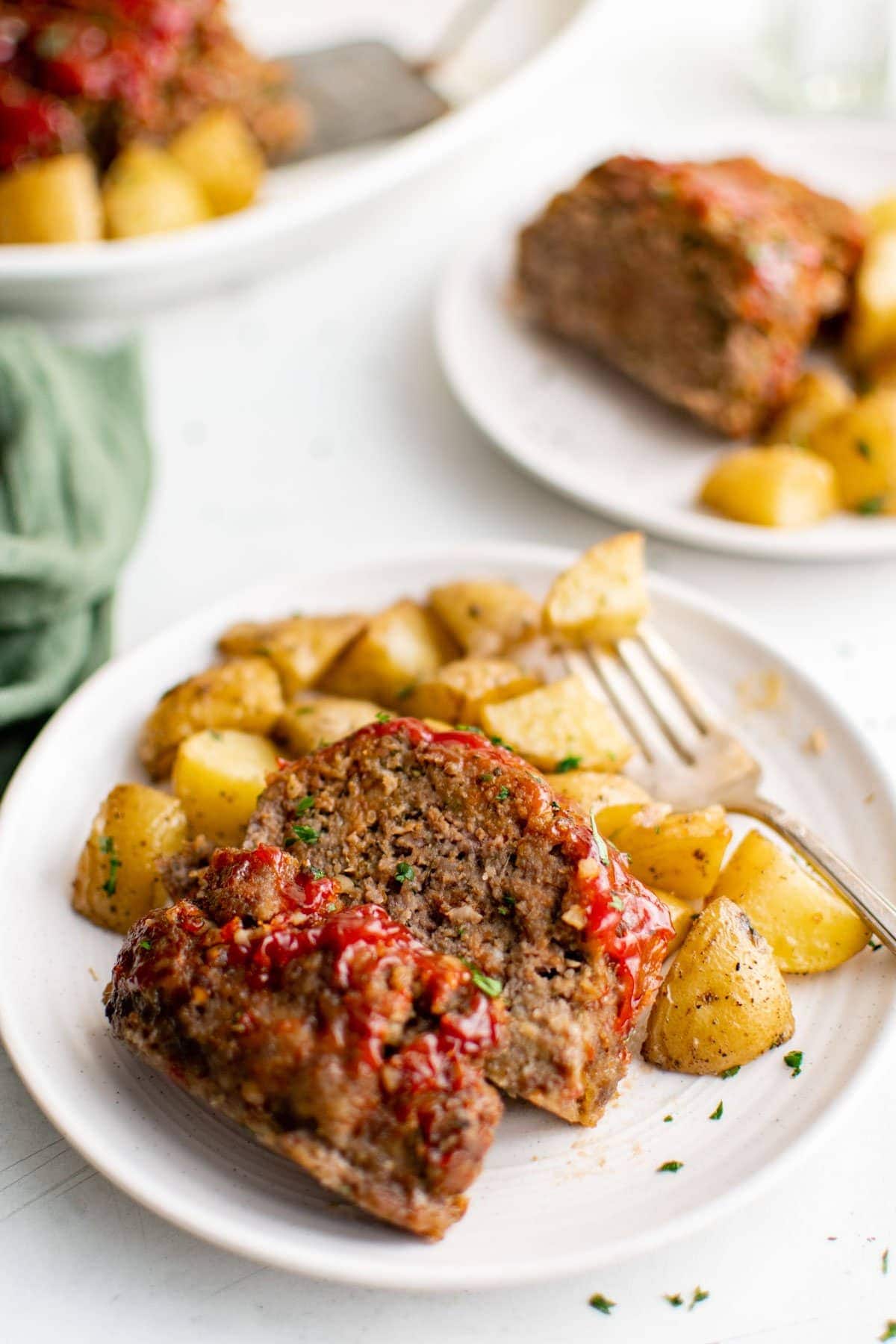 Pieces of glazed meatloaf and diced potatoes on a white plate.