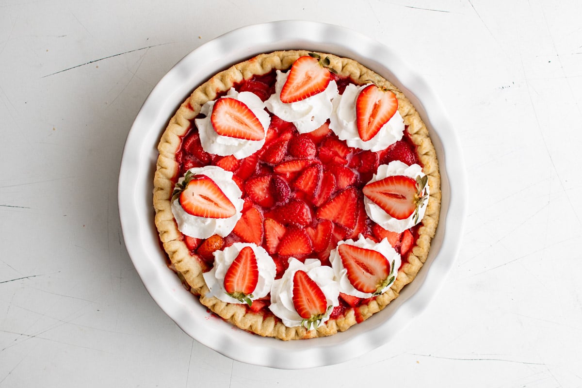 strawberries and whipped cream on top of a pie crust filled with strawberries and jello