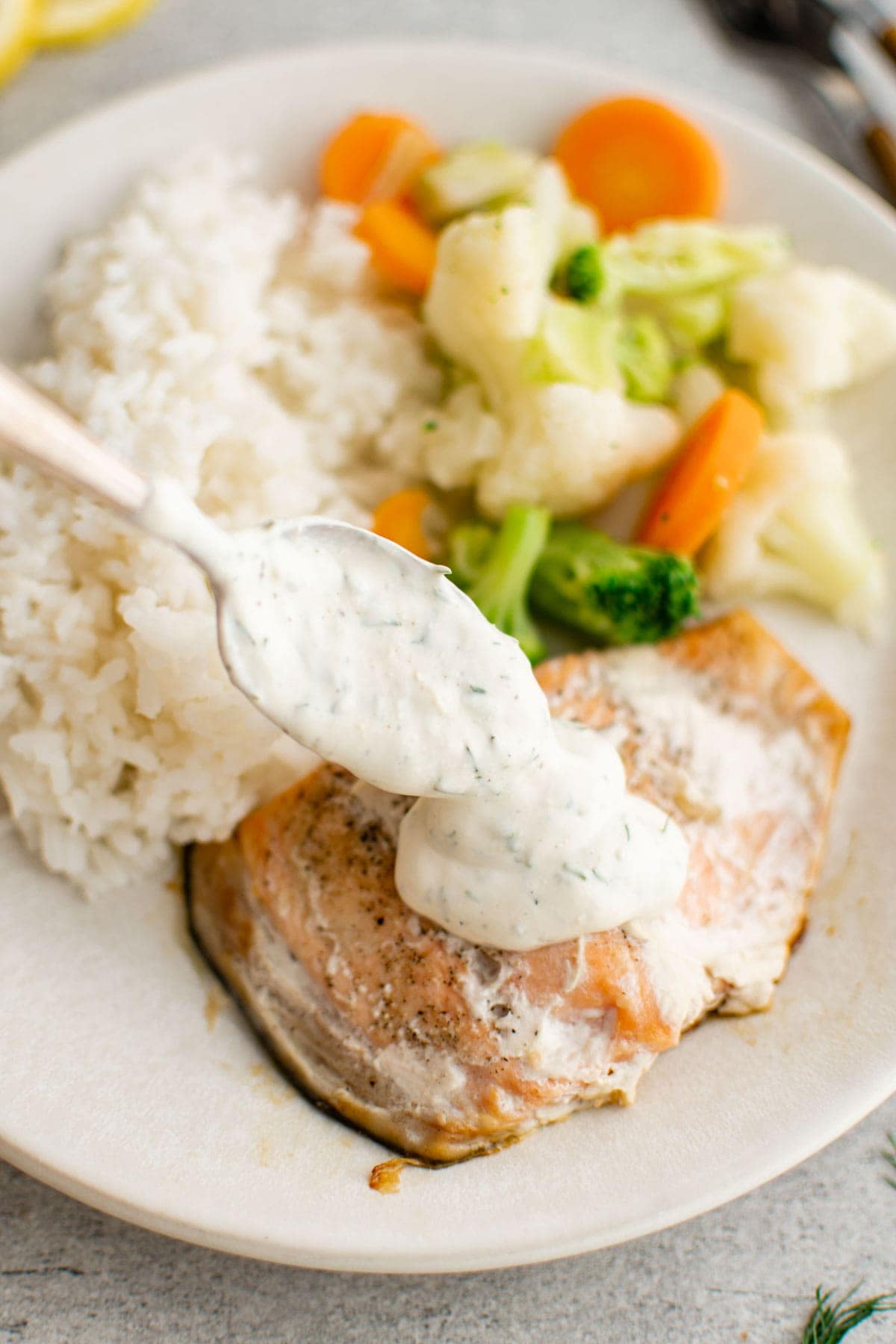 Spoon dill sauce onto a piece of salmon on a white plate. 