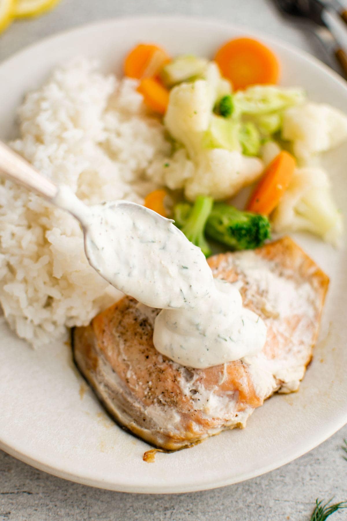 Spoon dill sauce onto a piece of salmon on a white plate.