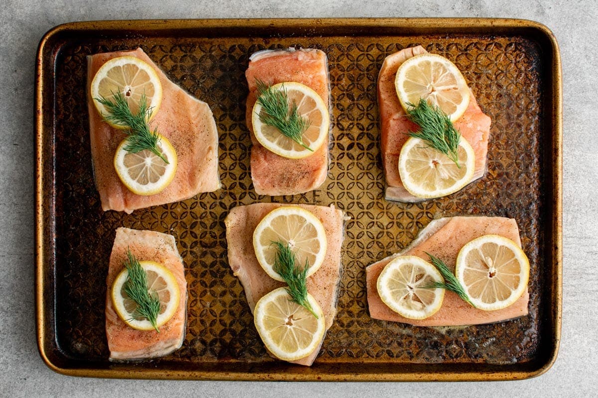 Fresh salmon on a baking sheet with sliced lemons and fresh dill. 