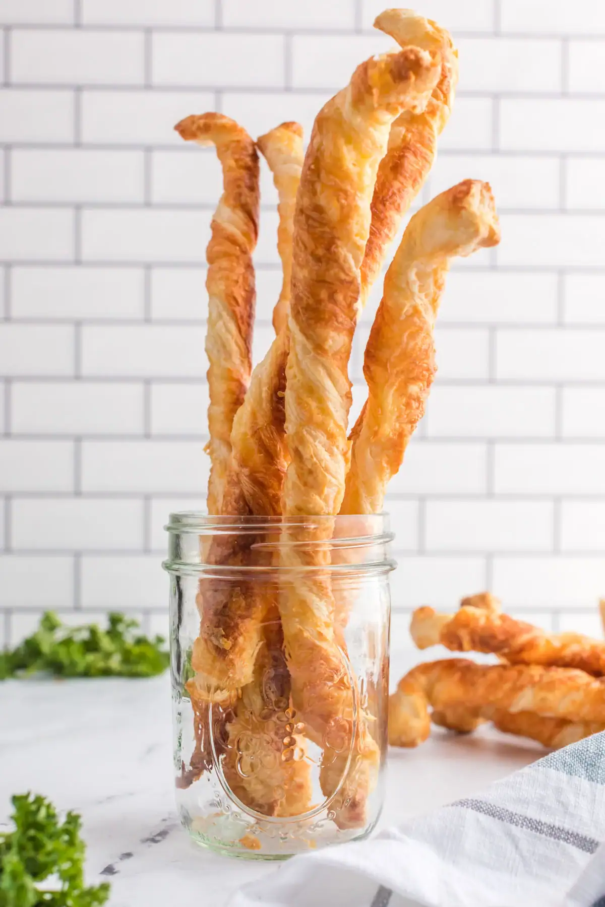 Puff pastry cheese straws standing up in a clear glass jar.