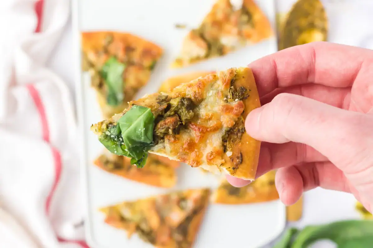 Hand holding up a piece of air fryer chicken pesto flatbread.