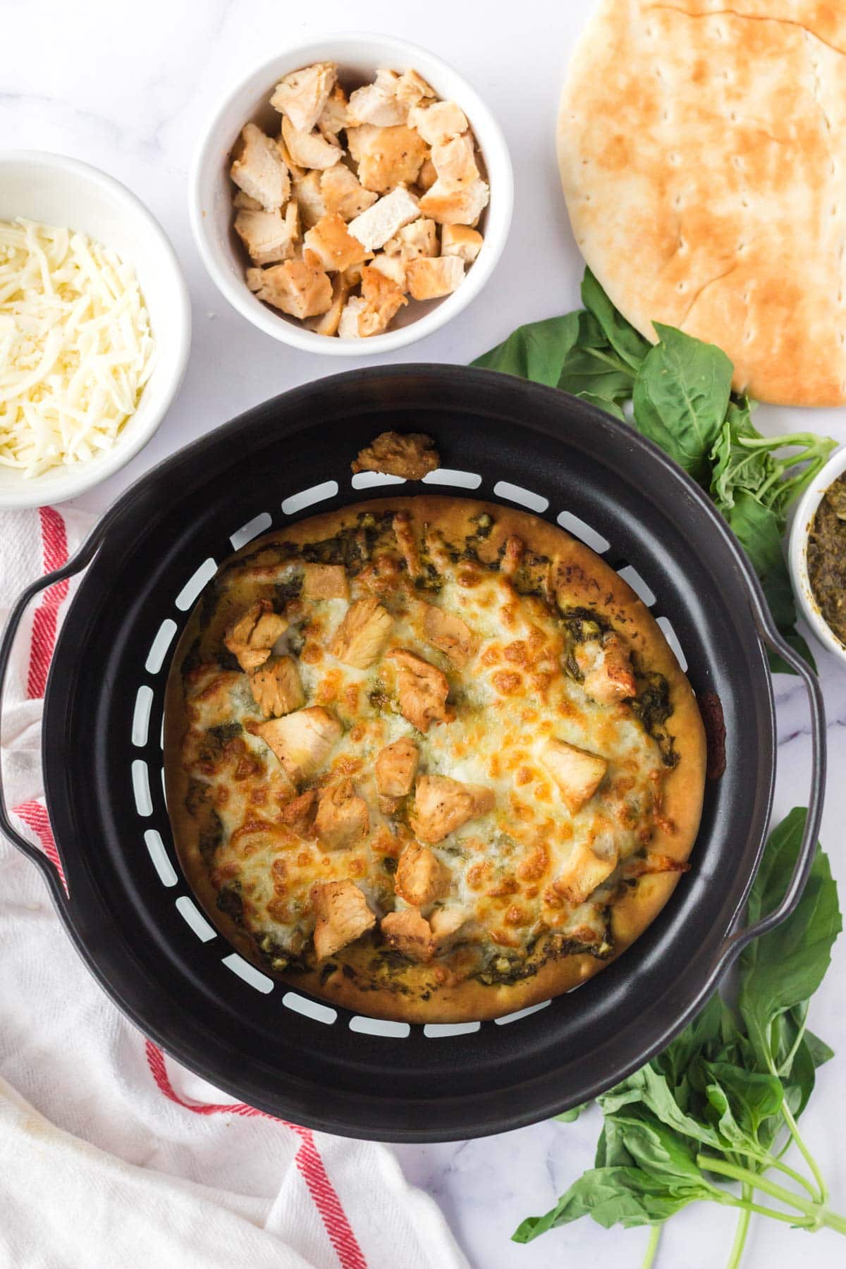 Cooked chicken pesto flatbread in an air fryer basket.
