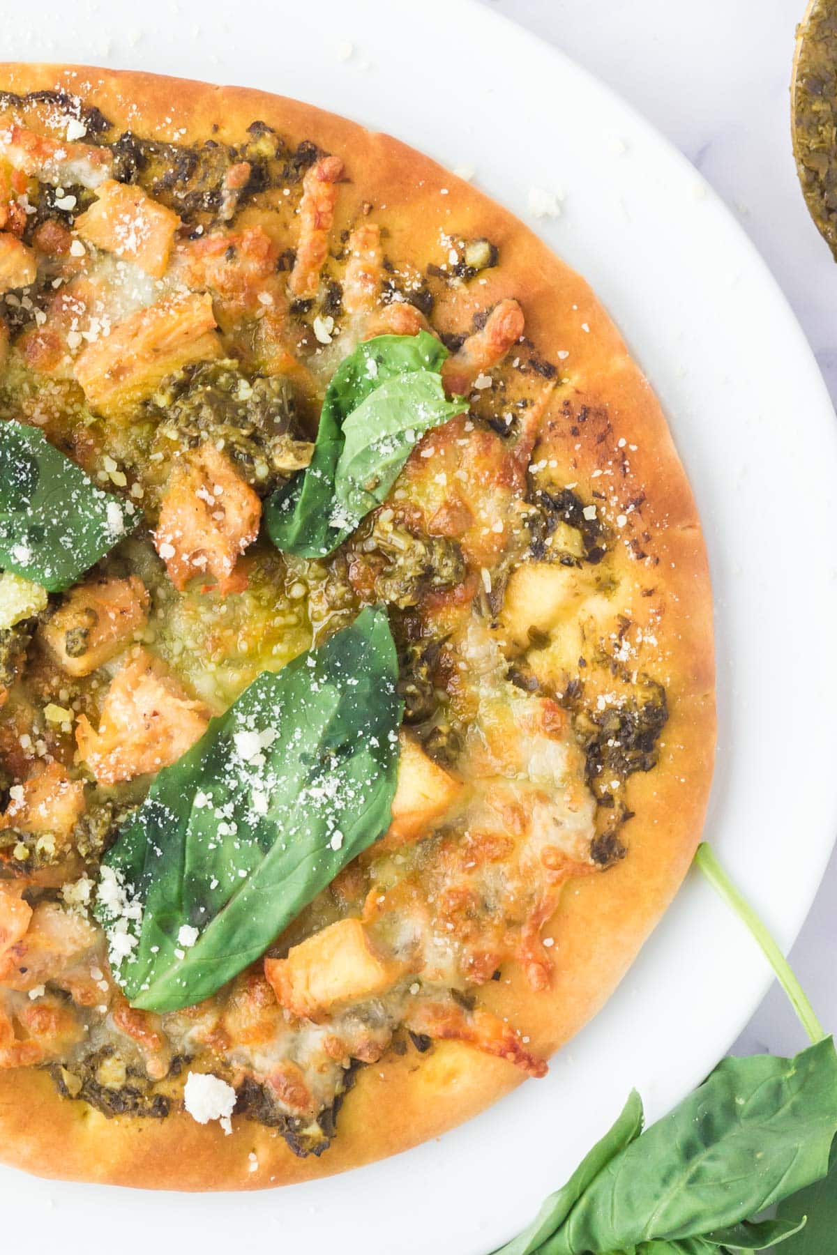 Air fryer pesto chicken flatbread on with fresh basil leaves on top.