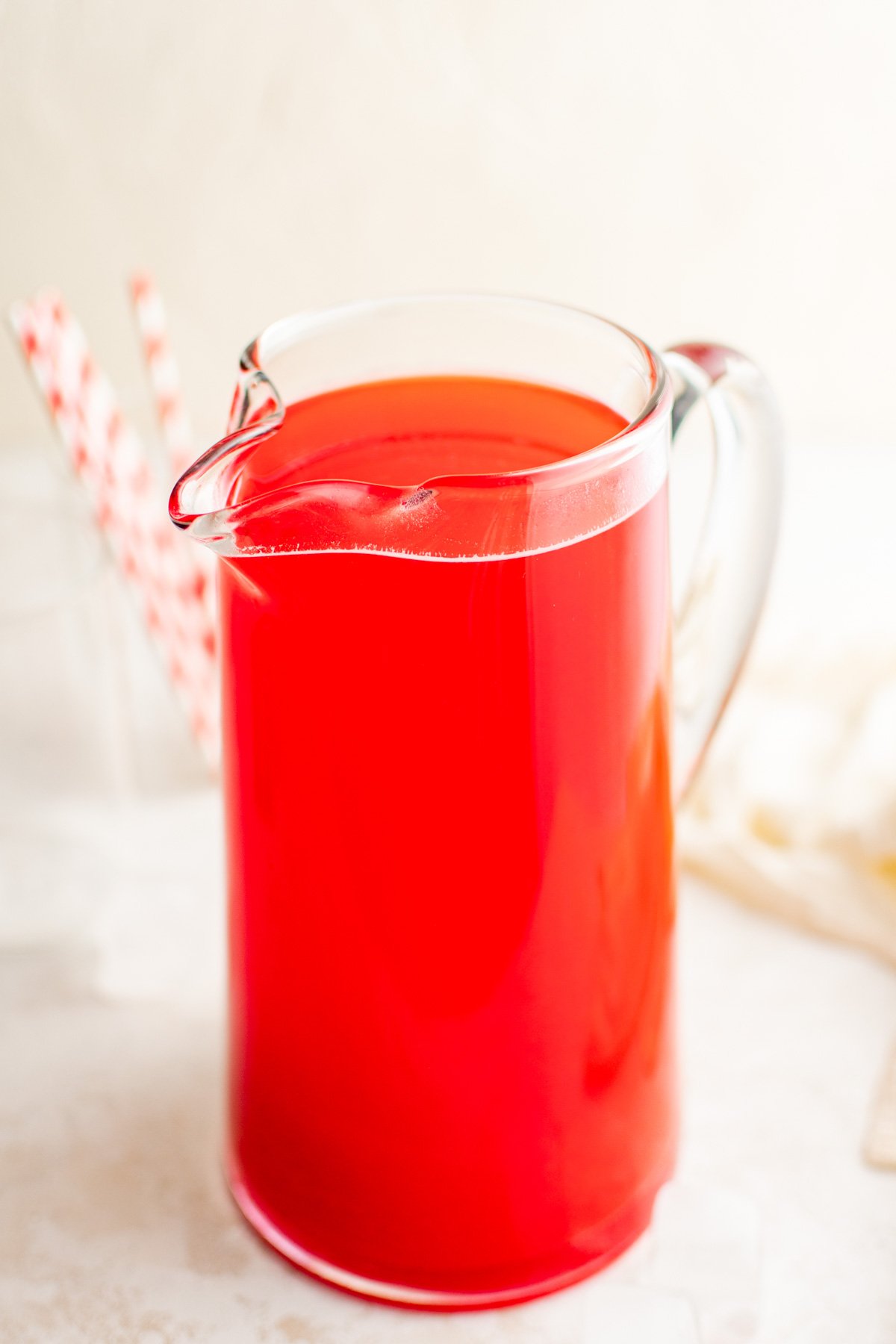 Hawaiian punch in a glass pitcher with red striped straws.