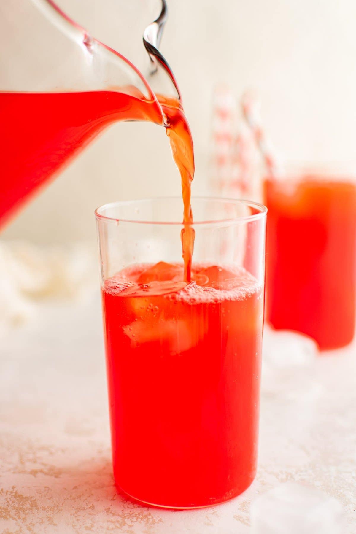 Red punch being poured into a glass from a glass pitcher. 