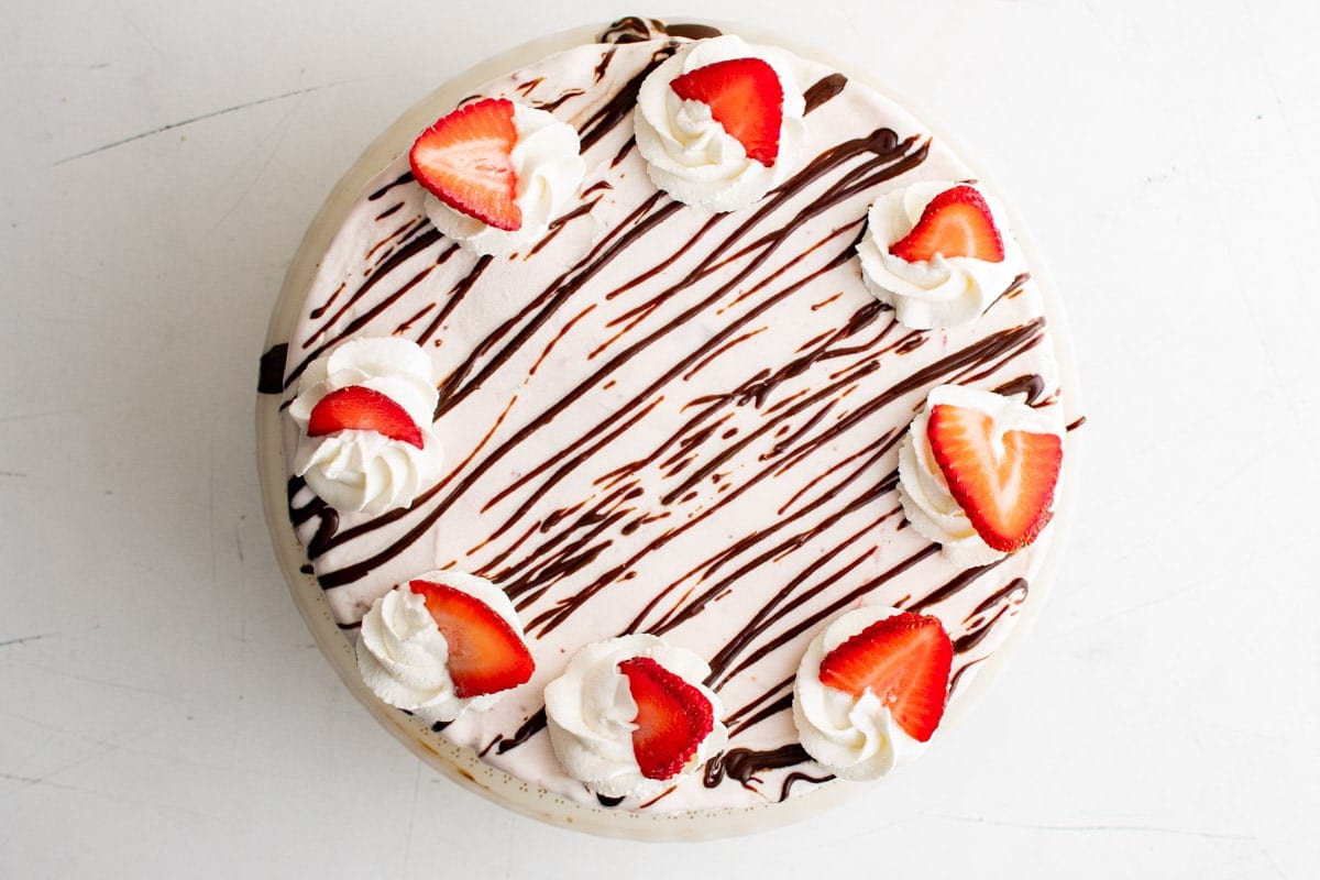 to top of an ice cream cake with whipped cream, fudge and fresh strawberries