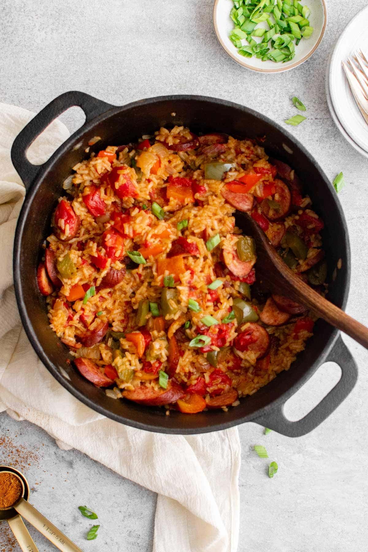 Cajun sausage and rice with sliced green onions on top, in a black pot and with a wooden spoon.