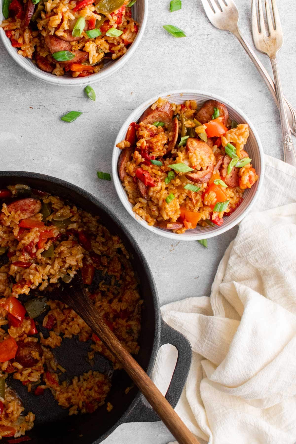 Black pot, two white bowls with sausage and rice, white napkin and forks.