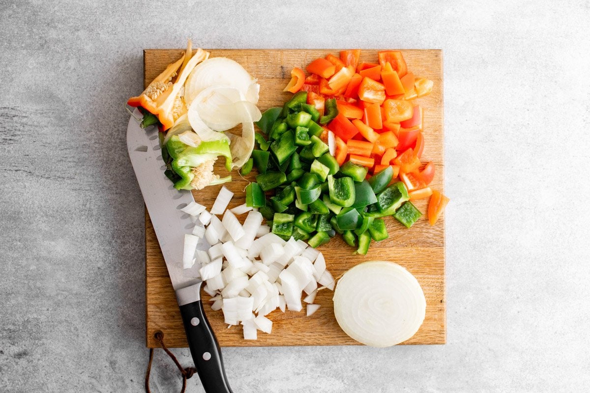 wooden cutting board with chopped onion, red pepper and green pepper and a knife.